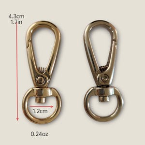 May include: Two gold-toned metal swivel clasps, each measuring 1.7 inches in length and 1.2 inches in width. The clasps are designed for attaching to bags, straps, or other accessories.