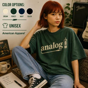 Puede incluir: Una camiseta unisex verde oscuro con la palabra "analog" impresa en blanco, junto con un gráfico de un amplificador de válvulas. La camiseta es de American Apparel y está disponible en crema, verde bosque, azul marino y negro.