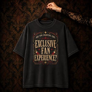 May include: A black short-sleeve t-shirt featuring a vintage-style graphic print in gold and red. The text reads: ARE YOU ENJOYING THIS EXCLUSIVE FAN EXPERIENCE? The design includes decorative flourishes, stars, and two small spotlight icons.