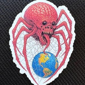 Puede incluir: Una pegatina que presenta una araña roja con forma de cerebro, con múltiples ojos y dientes afilados, sosteniendo un globo terráqueo en su telaraña. El globo es azul y amarillo. La obra de arte tiene un estilo ilustrativo detallado con un borde blanco.