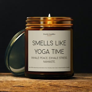 以下が含まれることがあります： 金色の蓋が付いた茶色のガラス製のキャンドルジャー。ラベルには「Smells Like Yoga Time」と「Inhale Peace. Exhale Stress. Namaste.」と書かれています。このキャンドルは100％天然大豆ワックスで作られており、環境に優しく、無毒で、アメリカで手作りされています。