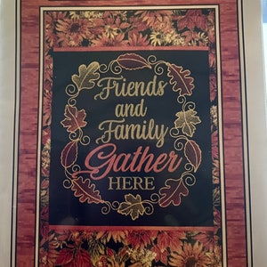May include: A wall hanging with an autumnal design. It features a wreath of leaves with the text "Friends and Family Gather Here" in gold and red lettering.