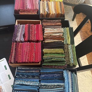 May include: A collection of fabric swatches in a range of colours, including pinks, reds, yellows, greens, and blues, arranged in rectangular boxes. The fabrics feature diverse patterns and textures, suitable for textile projects.