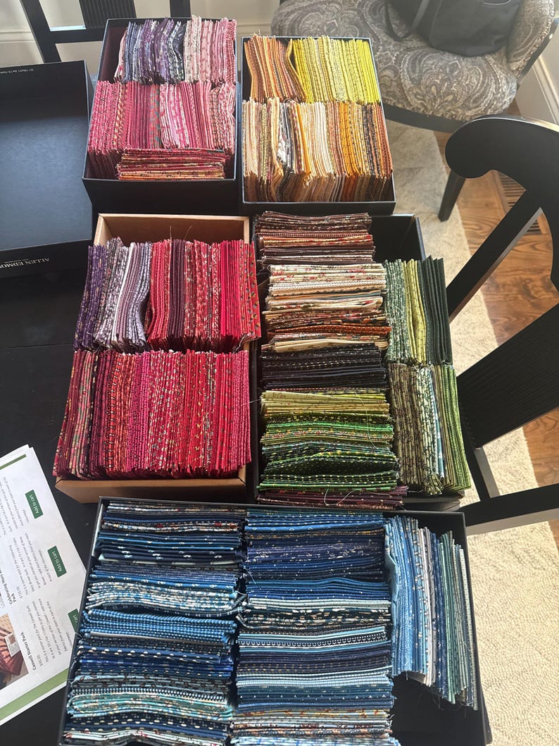 May include: A collection of fabric swatches in a range of colours, including pinks, reds, yellows, greens, and blues, arranged in rectangular boxes. The fabrics feature diverse patterns and textures, suitable for textile projects.