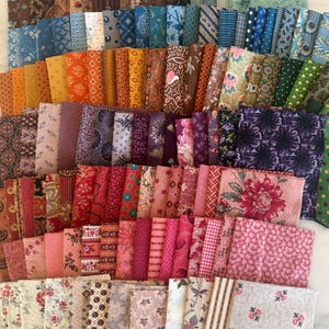 May include: A selection of fabric squares in diverse colours and patterns. The fabrics feature floral, paisley, and geometric designs in shades of blue, orange, pink, purple, and green. The squares are neatly stacked, displaying the variety of textiles.