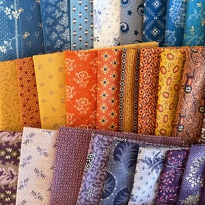 May include: A selection of folded fabric pieces in a variety of colours and patterns. The fabrics feature shades of blue, orange, yellow, and purple, with designs including floral, paisley, and geometric shapes. The fabrics are suitable for quilting or other craft projects.
