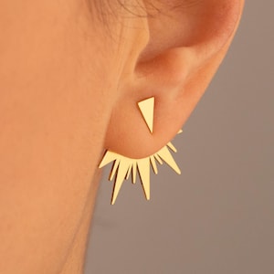 Puede incluir: Pendientes geométricos dorados con un diseño de estrella y un pequeño triángulo. Los pendientes se llevan en el lóbulo de la oreja y en el hélix.