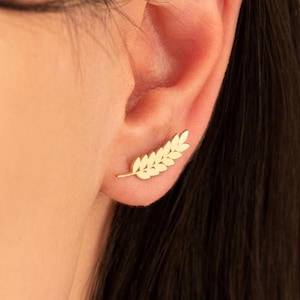 Puede incluir: Un pendiente de oro en forma de hoja con un diseño delicado. El pendiente se lleva en el lóbulo superior de la oreja.