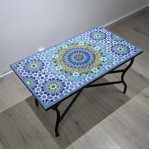 May include: Rectangular mosaic tile coffee table with a black metal frame. The tabletop features a blue, green, and orange geometric pattern. The table is approximately 122 cm long and 61 cm wide.