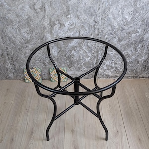 May include: A black metal table frame with a circular top and curved legs. The frame has a diameter of approximately 61 cm. The table is designed with a minimalist aesthetic, suitable for various interior styles.