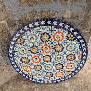 Pode incluir: Um azulejo redondo decorativo com um padrão geométrico em tons de azul, verde, amarelo, laranja e branco. O azulejo apresenta um desenho repetitivo de estrelas e círculos.