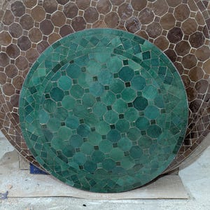 May include: A green and brown mosaic tile tabletop with a geometric pattern. The tabletop is round and has a diameter of approximately 76 cm.