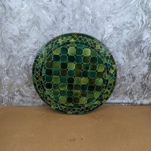 May include: Circular mosaic table top in shades of green. The design features a geometric pattern of squares and triangles. The mosaic is arranged in concentric circles. The table top would measure approximately 76 cm in diameter.