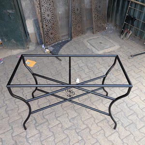 May include: Black metal table frame with a decorative design in the center. The frame is made of sturdy metal and has a rectangular shape.