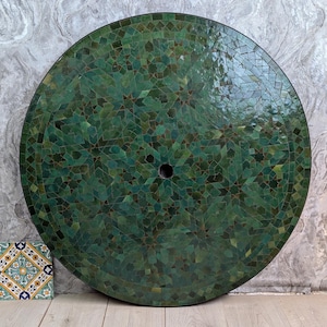 Pode incluir: Tampo de mesa redondo em mosaico nas cores verde escuro e verde-azulado. O mosaico é composto por pequenas telhas de formato irregular. O tampo tem um furo central e mede cerca de 91 cm de diâmetro.