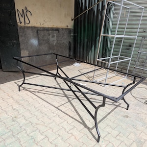 Peut inclure: Un cadre de table rectangulaire en métal noir doté d'un périmètre supérieur creux et de quatre pieds incurvés qui se rejoignent au niveau d'un support central en croix. La structure présente des volutes décoratives aux intersections.