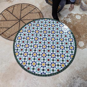 May include: A round table top with a geometric mosaic tile design. The tiles are white with blue, green, red, and yellow accents. The table top is approximately 76 cm in diameter.