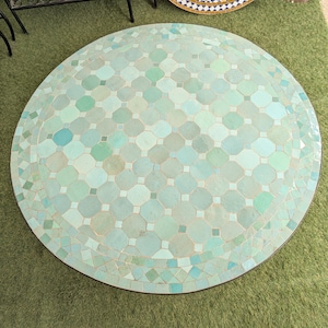 May include: A circular mosaic-tiled coffee table. The tiles are in shades of turquoise and green, arranged in a geometric pattern. The table has a dark brown edge. The table's diameter is approximately 100 cm.