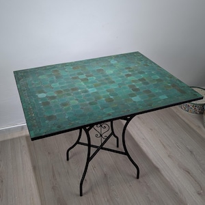 Könnte beinhalten: Quadratischer Gartentisch mit einer Mosaikplatte in Grün- und Blautönen. Der Tisch hat ein schwarzes Schmiedeeisen-Gestell mit dekorativen Schnörkeln. Der Tisch ist etwa 91 cm x 91 cm groß.