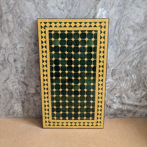 May include: A rectangular table with a mosaic tile top. The table features a dark green and yellow geometric pattern. The border is yellow with diamond shapes, and the center has a grid of green squares.