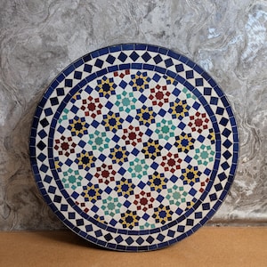 May include: A round, mosaic table top with a geometric pattern in shades of blue, red, yellow, and white.
