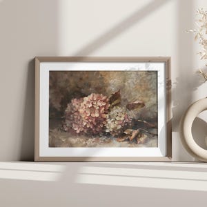 May include: A framed floral print featuring a cluster of pink and white hydrangeas with brown leaves. The artwork is displayed on a white surface, with a beige vase and decorative branch in the background.