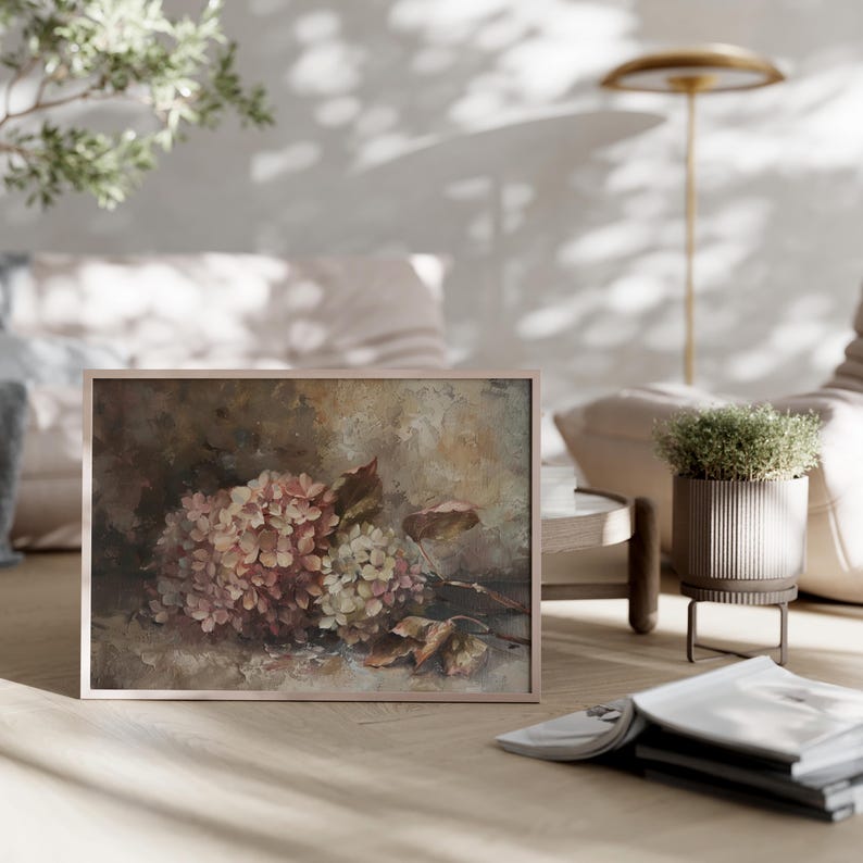 May include: A framed artwork featuring a still life of pink and white hydrangeas with brown leaves. The painting has a soft, muted color palette and is displayed on a wooden floor in a living room setting.