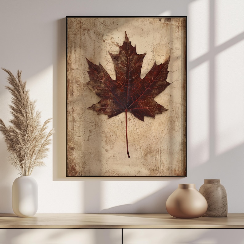 May include: A framed art print featuring a detailed close-up of a brown maple leaf. The leaf is centered on a textured, beige background with a distressed appearance. The artwork is displayed in a black frame, suitable for home decor.