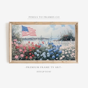 May include: A rectangular digital art display in a light wood frame featuring a landscape painting of a garden with red, blue, and white flowers, a white picket fence, and an American flag. Text reads PIXELS TO FRAMES CO, PREMIUM FRAME TV ART, FITS UP TO 85".