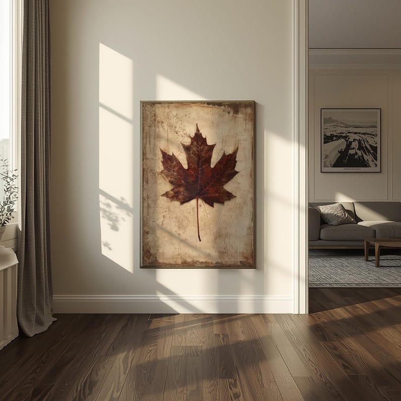 May include: A framed wall art piece featuring a large, detailed maple leaf in shades of brown and red. The leaf is centered on a textured, off-white background with a distressed, vintage aesthetic. The artwork is displayed in a well-lit room.