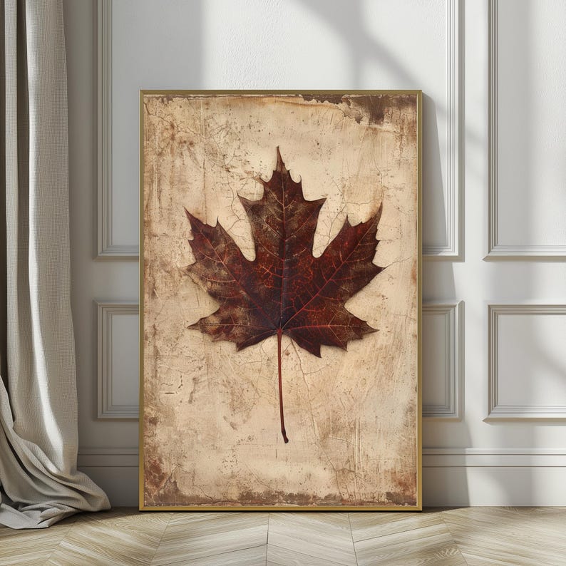 May include: A framed print featuring a detailed, dark brown maple leaf against a textured, beige background. The leaf's veins are visible, and the frame is gold. The artwork evokes a sense of autumn and nature.
