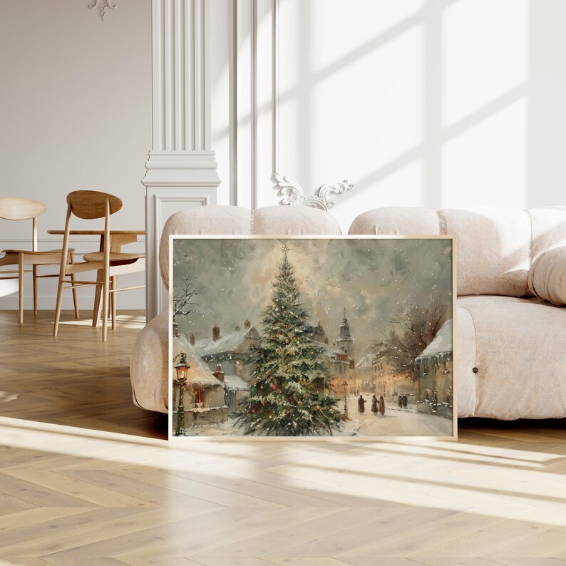 Peut inclure: Peinture encadr&eacute;e d'un paysage hivernal enneig&eacute; avec un grand sapin de No&euml;l. L'&oelig;uvre utilise une palette de couleurs douces de blancs, de gris et de verts, avec une lumi&egrave;re chaleureuse provenant des lampadaires et des fen&ecirc;tres des b&acirc;timents.