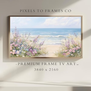 May include: Framed artwork depicting a serene beach scene. The painting features a sandy path leading to the ocean, framed by colorful wildflowers in shades of pink, purple, and white. The sky is a soft blue with fluffy white clouds.