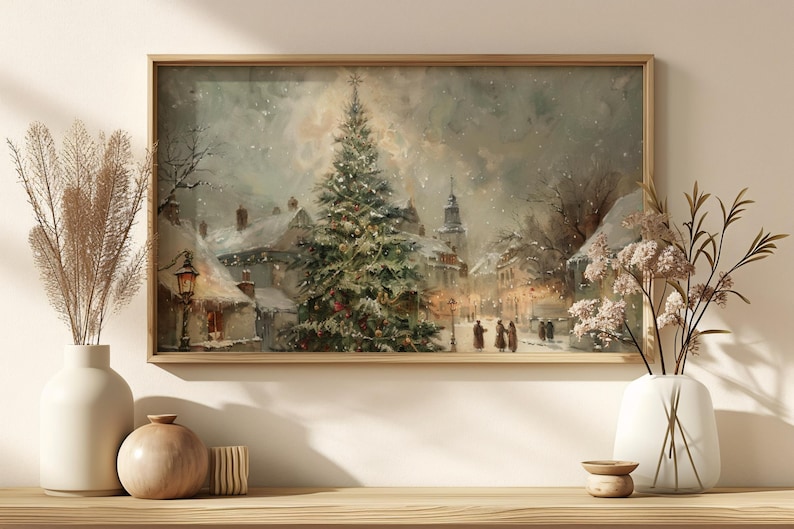 Peut inclure: Peinture encadr&eacute;e d'un paysage hivernal repr&eacute;sentant une place de ville enneig&eacute;e avec un sapin de No&euml;l d&eacute;cor&eacute;. L'&oelig;uvre pr&eacute;sente un clocher d'&eacute;glise, des lampadaires et des personnages marchant dans la neige, le tout dans des tons sourds.