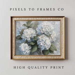 Op de afbeelding: Een ingelijste print met een bloemstilleven van witte en lichtblauwe hortensia's met groene bladeren. Het kunstwerk zit in een gouden, sierlijke lijst. De tekst bovenaan luidt "PIXELS TO FRAMES CO" en onderaan "HIGH QUALITY PRINT".