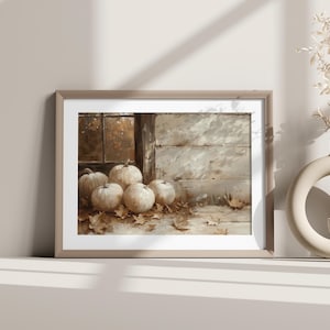 May include: A framed watercolor print featuring a still life of pumpkins and autumn leaves. The pumpkins are white and arranged on a wooden surface near a window. A beige vase with dried flowers is on the right.