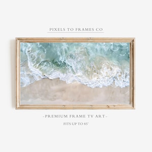 May include: A rectangular digital television display framed in light wood, showcasing an aerial view of turquoise ocean waves crashing onto a sandy beach. The text PIXELS TO FRAMES CO, PREMIUM FRAME TV ART, and FITS UP TO 85" is visible.