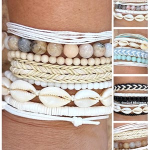 May include: A collection of stacked bracelets in various styles. The bracelets feature white, beige, and natural tones, with elements like woven textures, beads, and seashells. Some bracelets have a knotted design, while others use string.