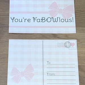 Pu&ograve; includere: Due cartoline con un motivo a quadretti rosa e bianco. Una carta ha un fiocco rosa e la scritta "You're FaBOwlous!". L'altra carta ha un fiocco rosa, le righe per "A:" e "Da:" e un francobollo.