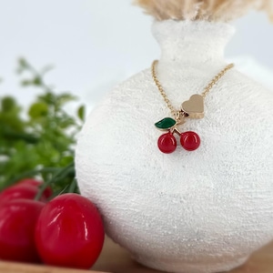 Op de afbeelding: Gouden ketting met een rode en groene kers-hanger en een gouden hart-hanger.