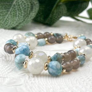 Peut inclure: Un bracelet multi-rangs composé d'un mélange de perles de pierre de lune blanche à facettes, de pierres de larimar bleu clair lisses et de perles d'agate grise polie, agrémenté de petites entretoises en métal doré et d'un fermoir doré.