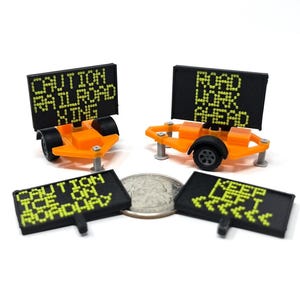 Pode incluir: Miniaturas de sinais de obras rodoviárias laranja com texto preto sobre fundo branco. Os sinais dizem "CAUTION RAILROAD XING", "ROAD WORK AHEAD", "CAUTION ICE ON ROADWAY" e "KEEP LEFT".