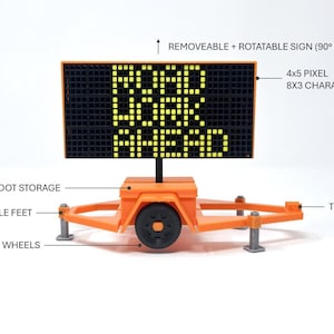 Pu&ograve; includere: Un cartello arancione di lavori stradali con la scritta "ROAD WORK AHEAD" visualizzata in pixel gialli. Il cartello &egrave; su un rimorchio con ruote, piedini rimovibili e un gancio di traino. Il cartello &egrave; rimovibile e ruotabile.