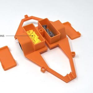 Pu&ograve; includere: Un organizer portaoggetti in plastica arancione con due scomparti, ciascuno con un coperchio. Uno scomparto contiene oggetti gialli, l'altro oggetti grigi. Il testo "STORAGE BINS" &egrave; visibile.
