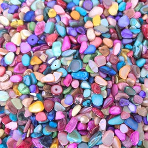 May include: A large collection of colourful, iridescent, and natural shell beads. The beads are various shapes and sizes, including oval, round, and teardrop.