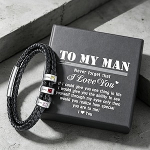 May include: Black braided leather bracelet with three silver name beads and a magnetic clasp. The bracelet is displayed next to a gray box with the text "TO MY MAN" and "I Love You".