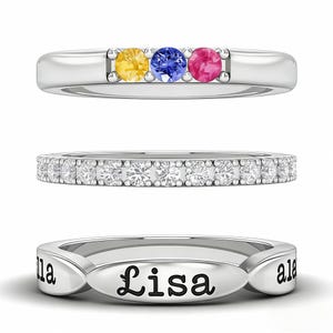 May include: Three silver rings. The top ring features yellow, blue, and pink gemstones. The middle ring is set with a row of clear gemstones. The bottom ring is engraved with the name "Lisa".