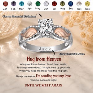 May include: A silver ring with a large, clear gemstone and rose gold accents. The ring features a wing design on each side of the gemstone. The word "Jack" is engraved on the band. The text "Hug from Heaven" is also visible.