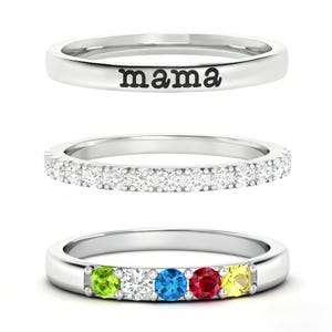 May include: Three silver rings. The top ring has the word "mama" engraved on it. The middle ring is encrusted with small, clear stones. The bottom ring has five colored gemstones: green, white, blue, red, and yellow.