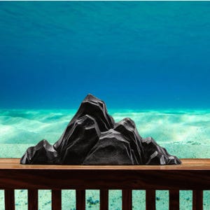 Puede incluir: Decoración de acuario negra y texturizada con forma de cordillera. La formación rocosa decorativa se encuentra sobre una superficie de madera, con una escena submarina de fondo. La montaña tiene picos afilados y una superficie rugosa.